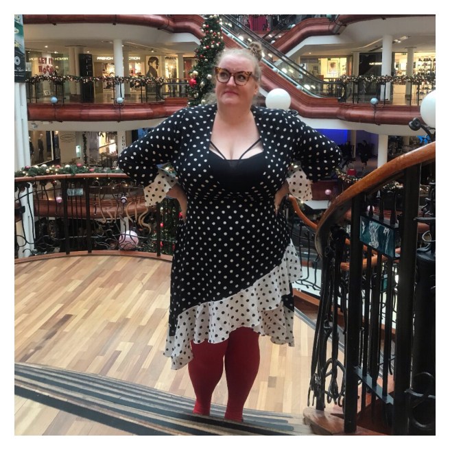 Plus size women on stair case on polka dot dress. Xmas decorations on background 