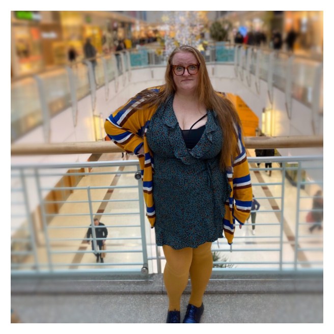 Plus sized women with long rescues hair in leopard print dress standing in front of Xmas lights
