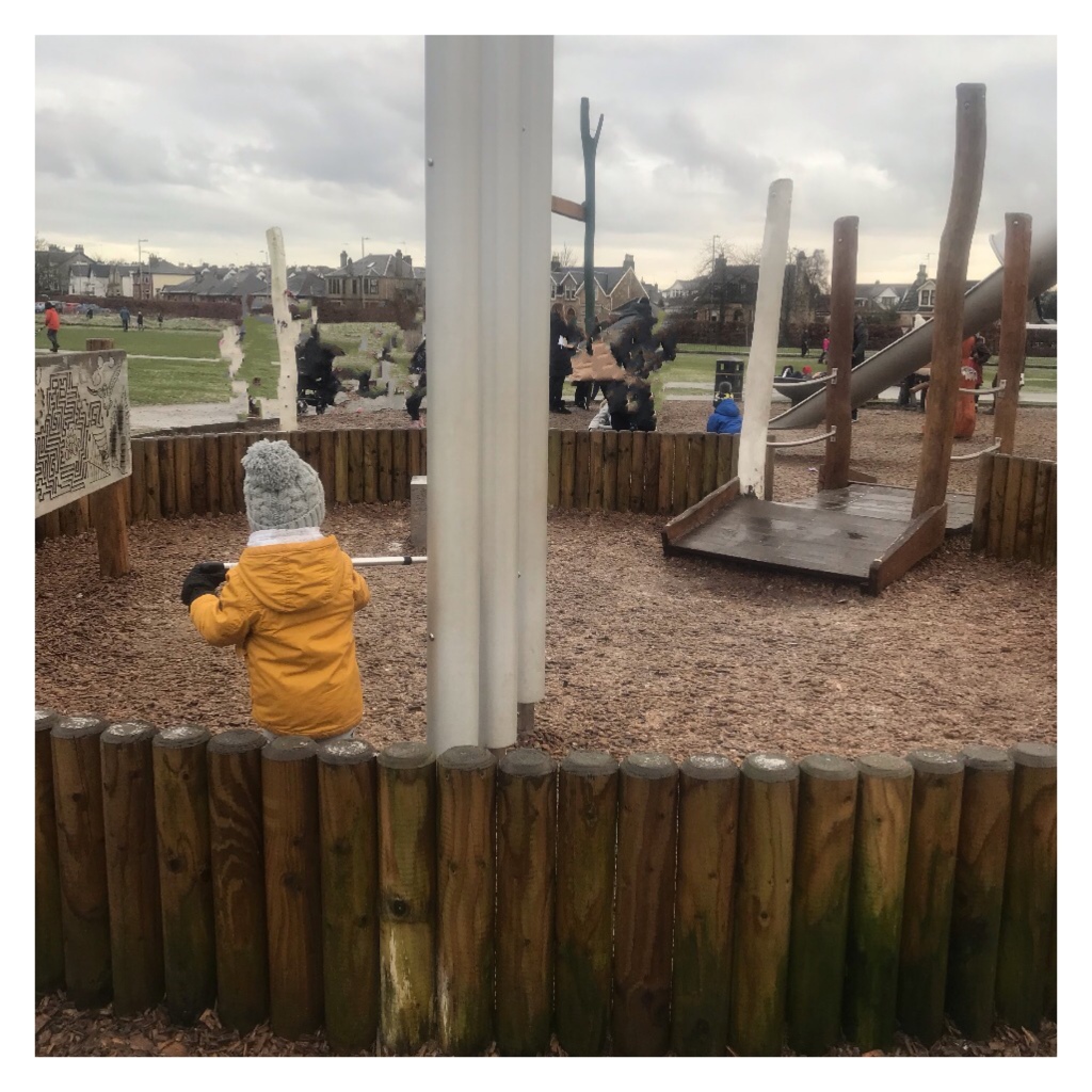 Toddler in coat & Woolly hat in playpark