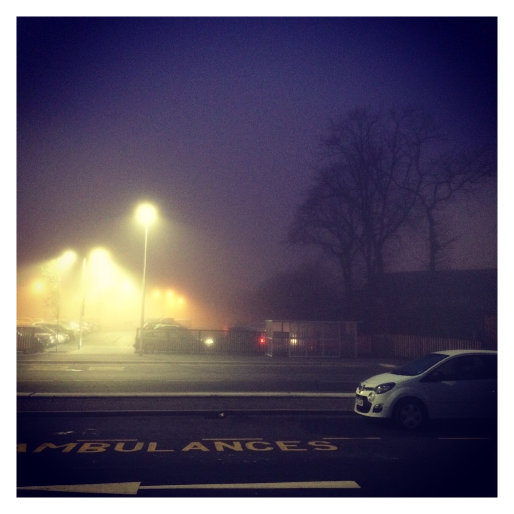 Foggy picture of cars outside hospital. Words ambulance only painted on ground 