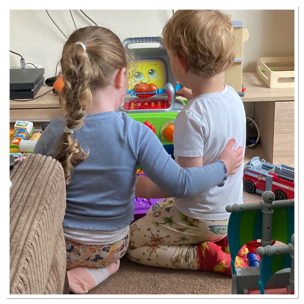 Two toddlers kneeling in floor  playing.  One with arm around the other 