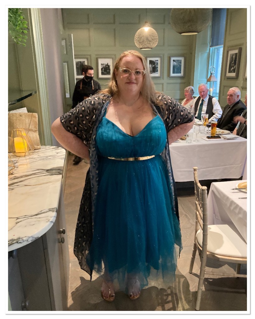 ly is wearing green sparkly swing dress with gold belt & sandals 