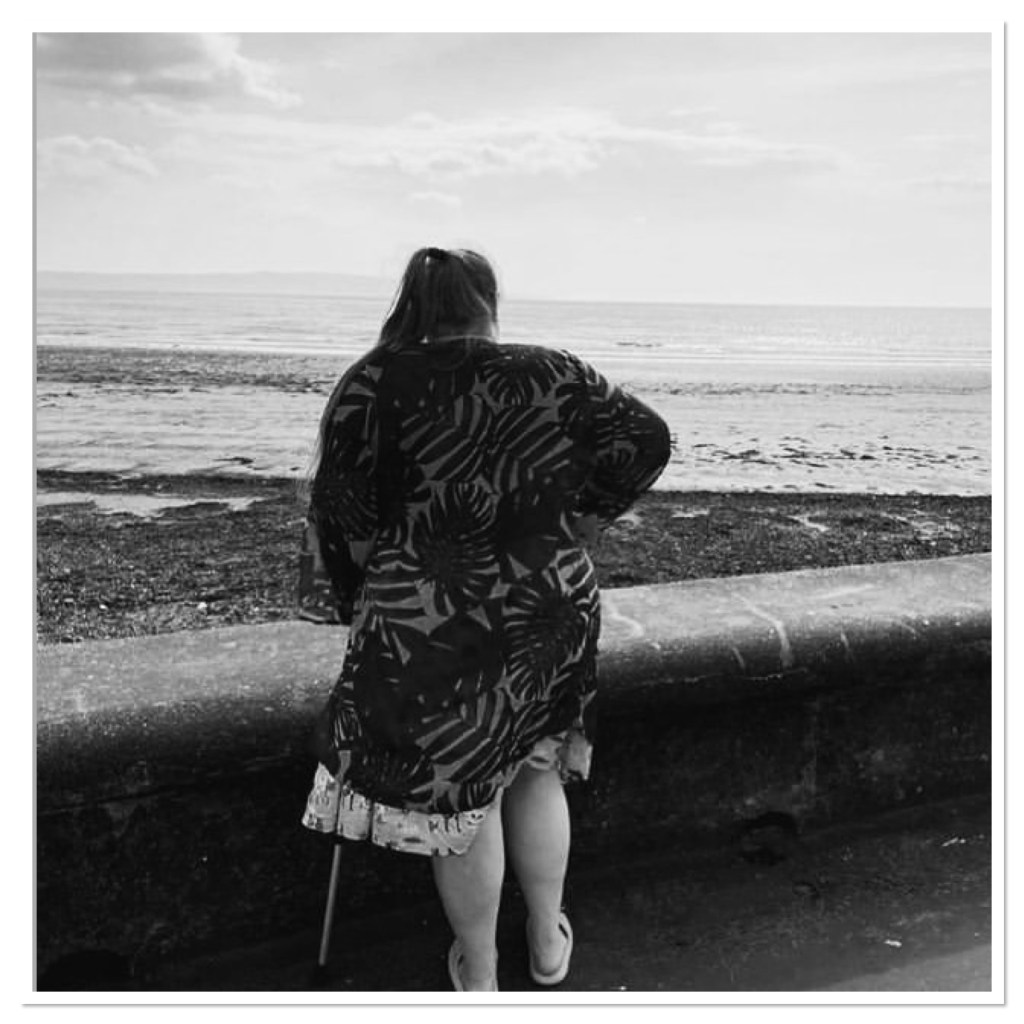 Black & white image of ly looking out over a beach. Taken from behind. 