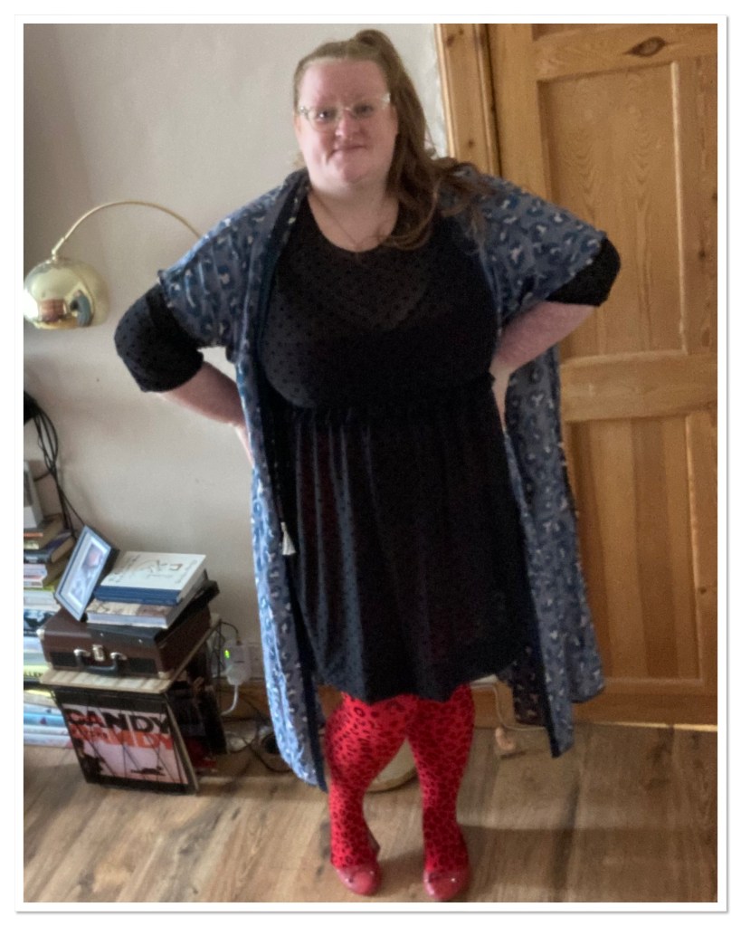 ly is standing with her hands on her hips wearing red leopard tights & a sheer black dress