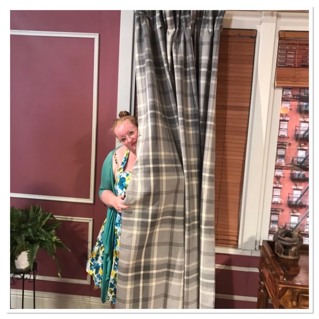 Ly is wearing floral dress and peeping out from behind a curtain. 