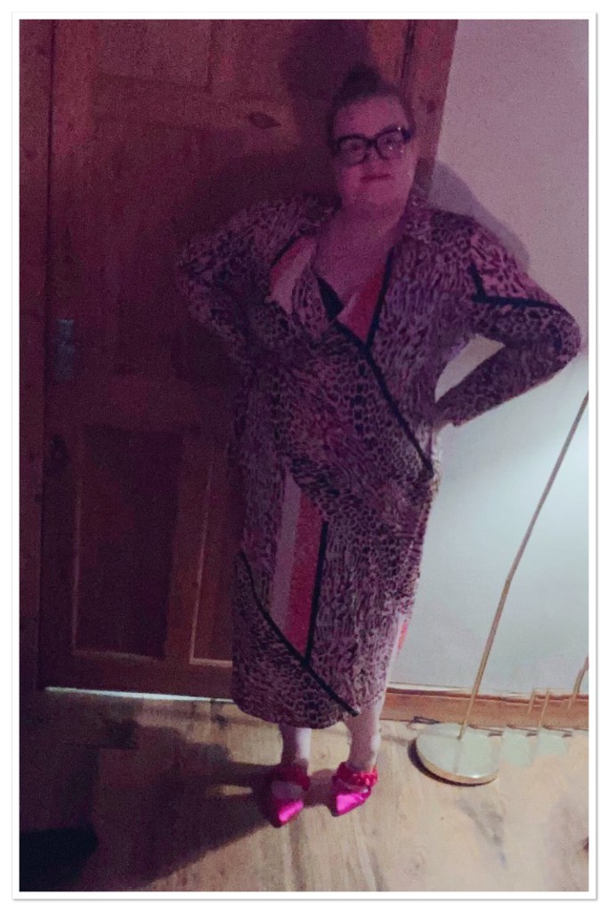 Ly is in her living with her hands on her hips. She is wearing a leopard print calf length dress 