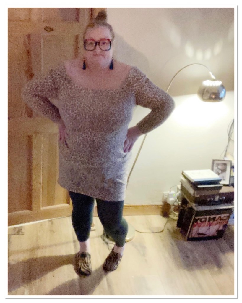 Ly is wearing a leopard print dress, tights & clogs. She is standing with her hands on her hips. 