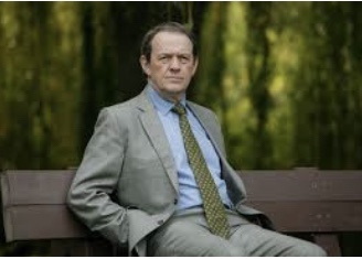 Man in light coloured suit  sitting on park bench with hands in his pockets 