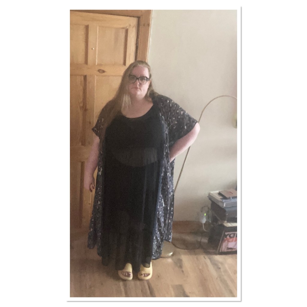 ly is standing with one hand on hip wearing sheer black maxi dress