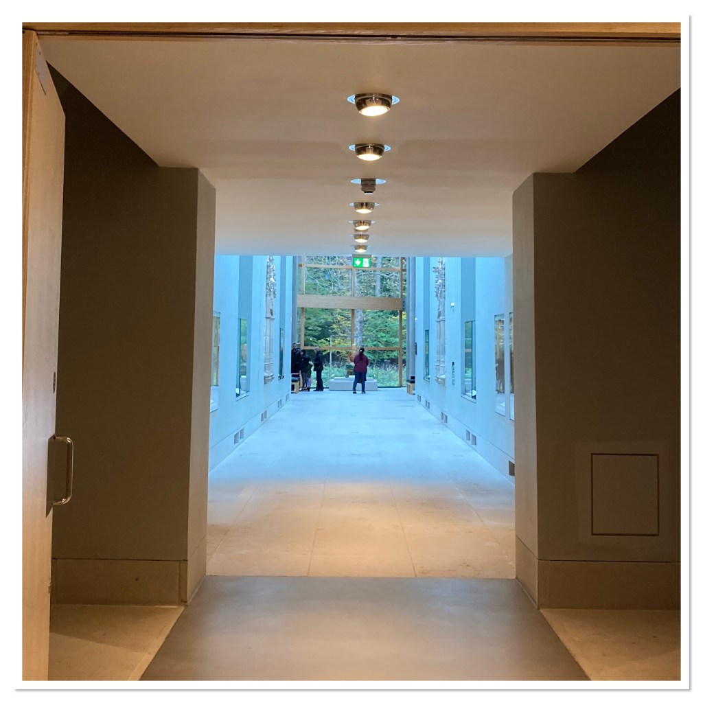 Long white corridor leading to huge window looking out to forest 