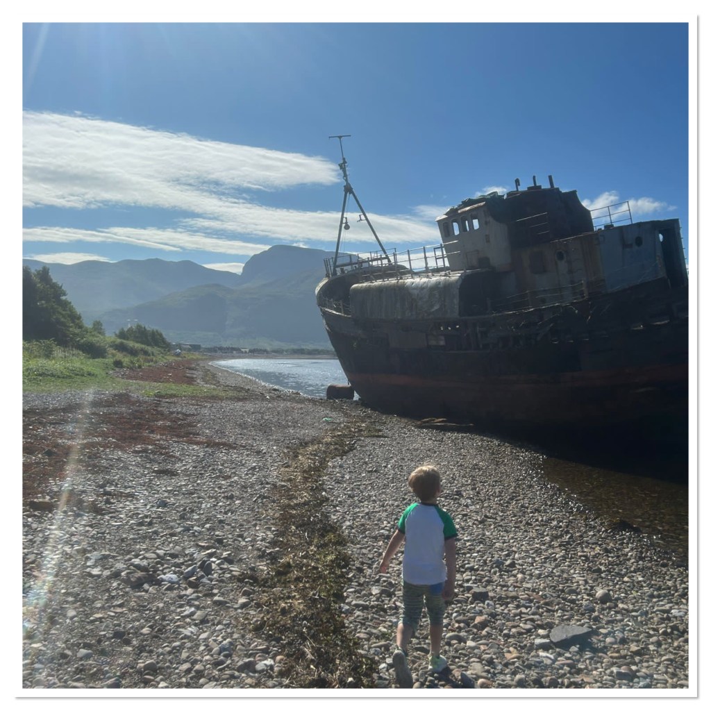 A little boy looking at a shipwreck on a beach 